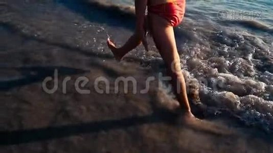 一个赤脚的小女孩在晚阳的温暖光线下沿着大海在潮湿的沙子上奔跑的缓慢运动。 粗心和粗心视频