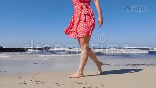 年轻女子的腿在沙滩上行走，海浪很大。 穿着红色裙子的年轻女子在塞浦路斯海滩漫步视频