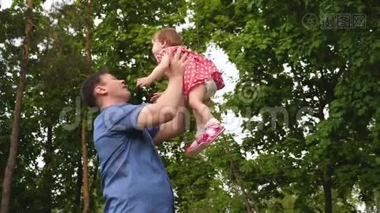 年轻的爸爸和宝宝在户外玩耍时一起笑。 女孩在父母手边跳着，微笑着。 慢慢视频
