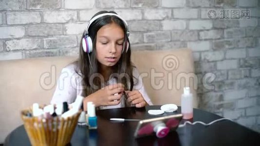 可爱的女孩戴着耳机，一边听着电话里的音乐，一边在家做指甲，免费复印空间视频