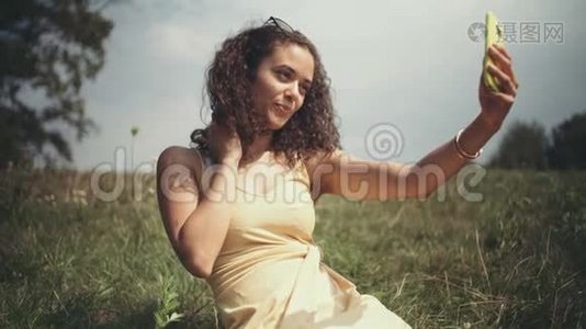 年轻漂亮的女人坐在草地上打电话自拍。视频
