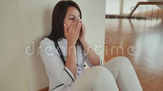 年轻的女医生坐在医院的地板上哭泣。视频