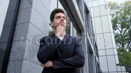 城市中年轻成功的沉思商人的肖像。 在办公楼背景上穿商务夹克的人。 帅哥视频