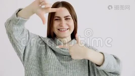 美丽的欧洲女孩，穿着一件温暖的毛衣，正对着白色的墙摆姿势。 欢笑和拍照视频