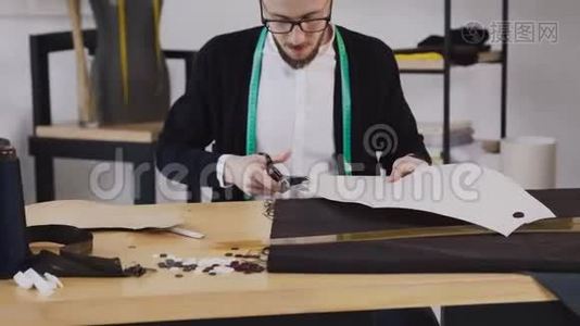 一位年轻的设计师或裁缝坐在工作室的缝纫桌旁，用剪刀雕刻出一幅素描。视频