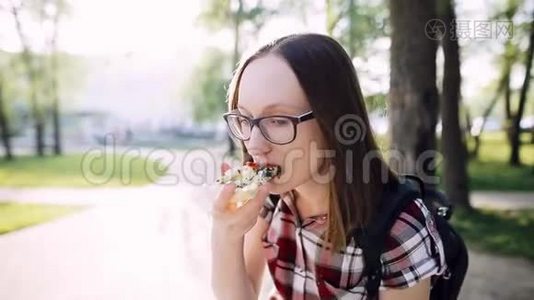 戴眼镜的白人时髦女孩吃一片带菠菜的素食披萨。视频