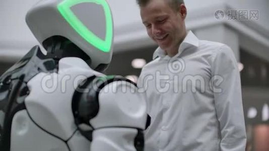 一个穿衬衫的男人和一个白色机器人交流，他问问题，用手指按屏幕。视频