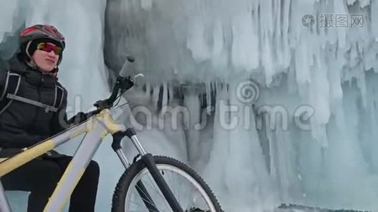 人们坐在冰窟附近的自行车旁。 有冰洞和冰柱的岩石非常美丽。 骑自行车的是视频