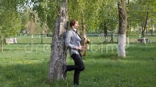 年轻人演奏萨克斯管。 人站在绿草上，走在桦树之间。视频