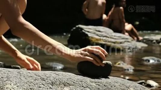 女演员在游客的背景下，在一条山河上的鹅卵石上站着一个凯恩的特写镜头，塔视频