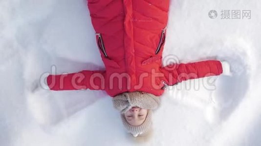 快乐的女孩躺在雪地上展示天使。 一个穿外套的漂亮女孩躺在雪地上，张开双臂。视频