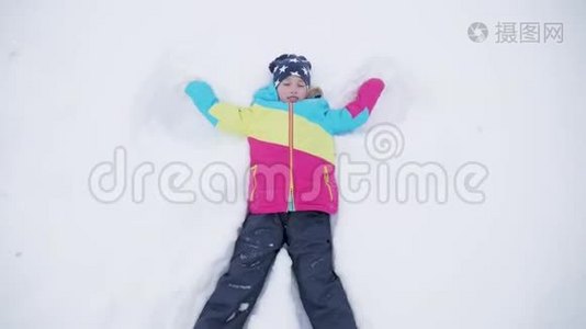 快乐的女孩躺在雪地上展示天使。 一个穿外套的漂亮女孩躺在雪地上，张开双臂。视频