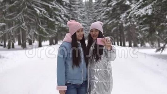 两个女朋友站在冬天的森林里，用智能手机自拍视频