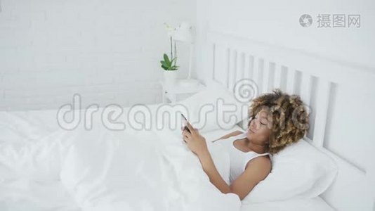 微笑的女人在床上用电话放松视频