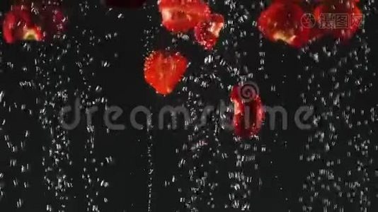 落下来的新鲜红色草莓片溅到闪闪发光的水在黑色的背景。 关门视频