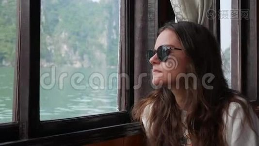 一位年轻女子穿着白色毛衣和太阳镜坐在船里，正注视着海湾的美丽景色视频