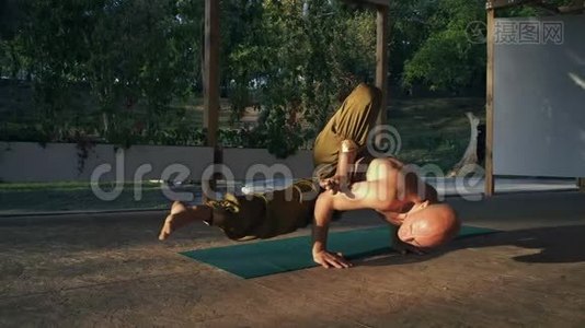 清晨，在城市公园，光着身子的年轻赤脚男子在木助手上做瑜伽视频