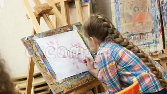 小女孩艺术家在画架上画画。 绘制过程：画笔和画布的特写..视频