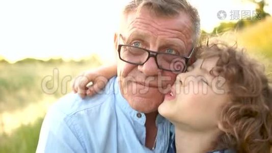 一个卷曲的小学生和他的祖父的特写肖像。 那个人高兴地拥抱了他的孙子。 家庭假期快乐视频