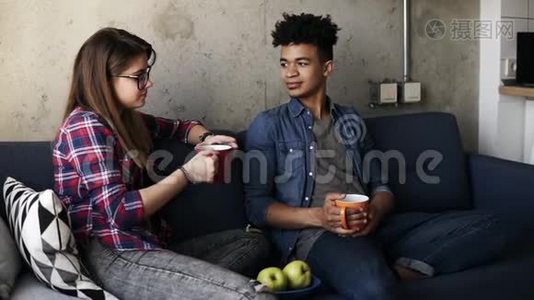 可爱的年轻夫妇，迷人的白种人女孩和她英俊的穆拉托男友坐在沙发上喝茶视频