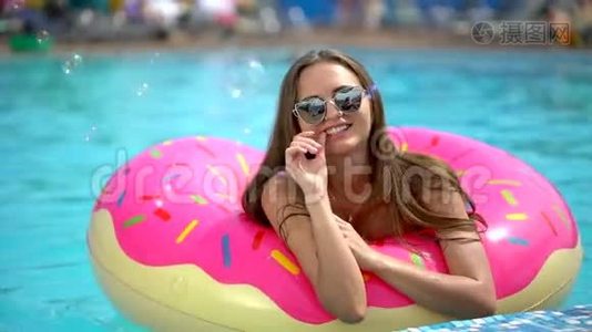 夏天美丽的年轻女子。 比基尼女孩哈文在洒满甜甜圈的乐趣在游泳池，假期，夏天，夏天视频