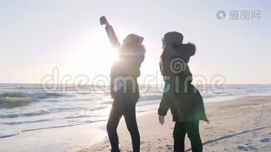 积极的娱乐活动，积极的女孩玩得开心，在阳光下在海洋海岸的手机上自拍。视频