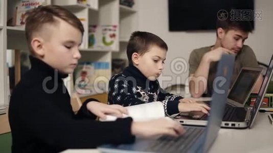 两个小男孩在笔记本电脑键盘上打字，而他们的男程序员老师正坐在附近。视频