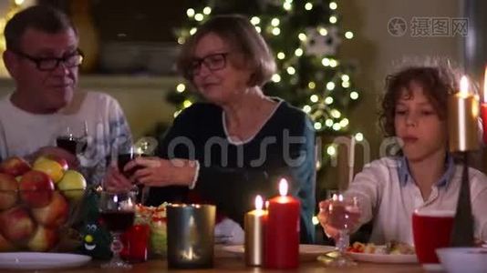 大家庭聚集在圣诞餐桌前，一家人聚餐.. 大人从杯子里喝红酒，男孩喝水视频