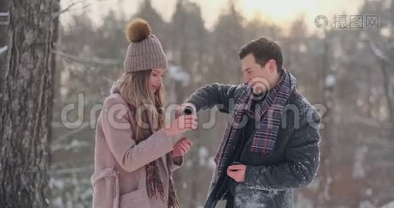 情侣在冬天的森林里喝热水瓶里的茶。 冬天公园里穿外套的时髦男女视频
