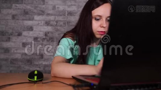 年轻女子看着笔记本电脑的显示器。 集中深色上衣，裸肩浏览，同时工作视频