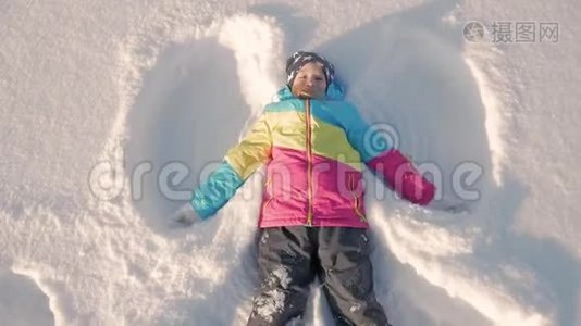 快乐的女孩躺在雪地上展示天使。 一个穿外套的漂亮女孩躺在雪地上，张开双臂。视频