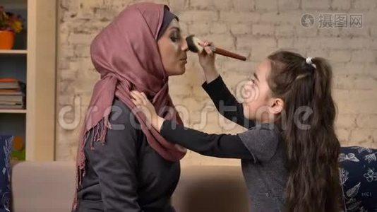 小女孩给她的穆斯林妈妈做了一个头巾的化妆，化妆刷，笑，微笑的家庭，懒散，家庭舒适视频