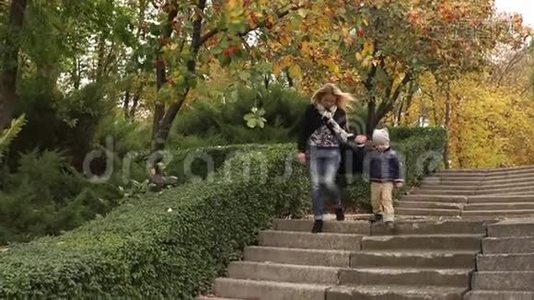 妈妈和儿子在秋天在公园下楼梯。视频