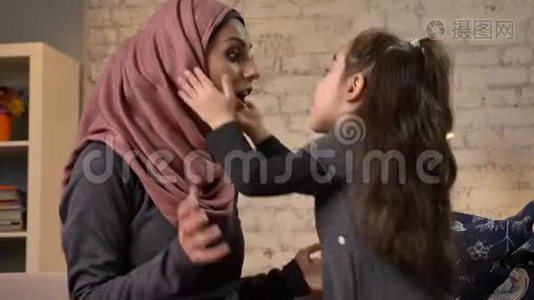 一个小女孩用头巾亲吻她的母亲，坐在沙发上，家庭，家庭，家庭舒适的概念，母亲和女儿。 50视频