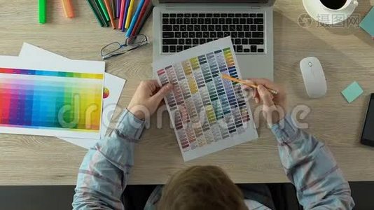 设计师选择调色板上的颜色，并在办公室的笔记本电脑上工作，顶部视图视频