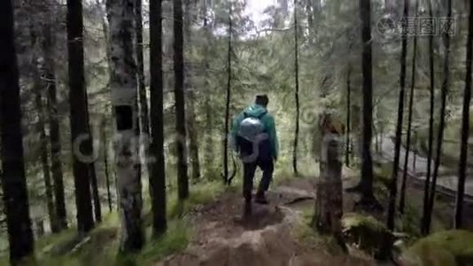 旅行者沿着森林小径漫步的后景。 库存录像。 带着背包和雨衣的旅行者走在崎岖的道路上视频