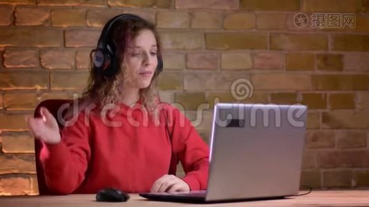 年轻女性博客作者的肖像，红色帽衫记录视频使用笔记本电脑在布里肯墙背景。视频