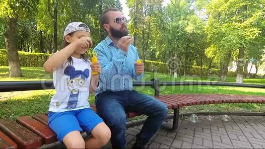 那个女孩和她爸爸坐在公园的长凳上。视频