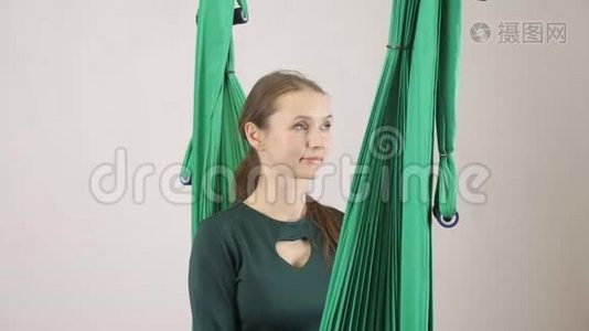 年轻的女人坐在吊床上微笑的女人展示你叫我标志。 空中航空飞行健身教练训练。 冥想视频
