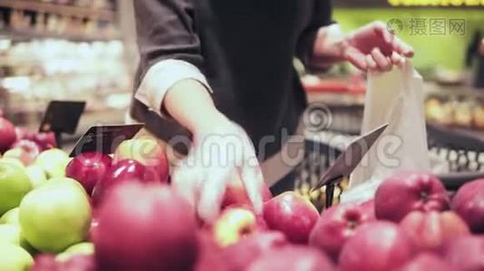 在杂货店买红苹果的女人。 女人用手在水果和蔬菜过道里摘苹果视频