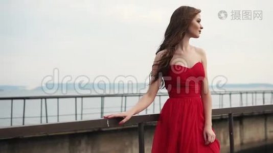 美丽的女人享受着凉风，吹拂着她鲜红的裙子和头发视频