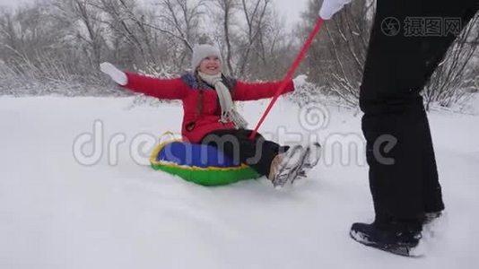 孩子和母亲在雪地里雪橇。 女儿和妈妈在圣诞节假期在冬季公园玩。 冬天视频