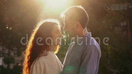 年轻漂亮的一对夫妇在秋天公园度过亲密的时光。 日落的光，太阳耀斑。 喜欢约会的情侣视频