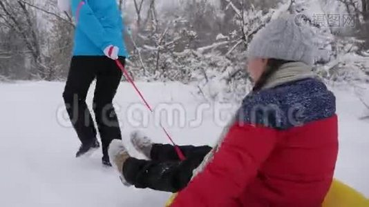 孩子和母亲在雪地里雪橇。 女儿和妈妈在圣诞节假期在冬季公园玩。 冬天视频