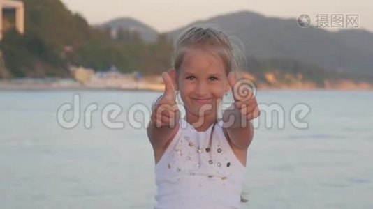 快乐的小女孩在海滩上，小女孩展示手势超级。 女孩的手用拇指向上完美的符号是好的，视频