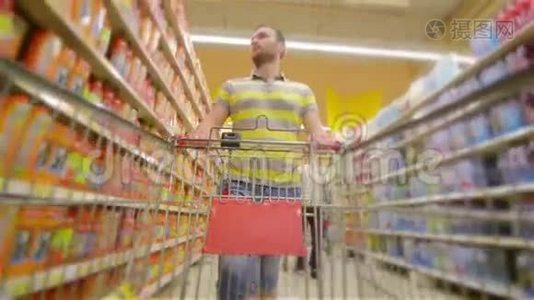 一个人带着满满的超市手推车，走近摄像机，开心地笑着，年轻人在超市里挑选产品视频