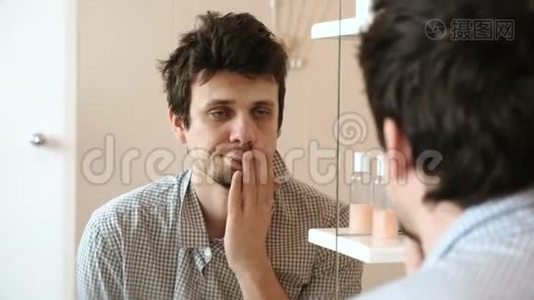 刚刚醒来的疲惫的男人看着镜子里的倒影，拍打着他的脸颊，直着他的头发视频