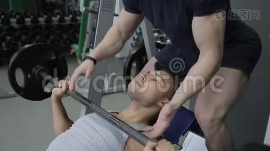 年轻的运动员正和他的教练一起在健身房做他在斜凳上的努力。视频