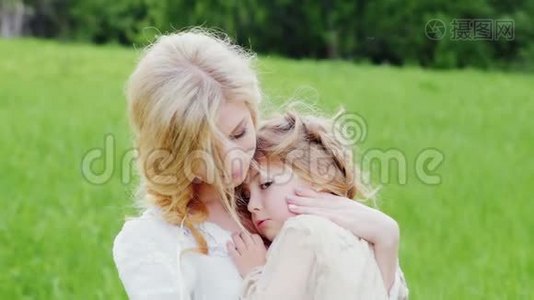 年轻的金发母亲在绿色的草坪上拥抱她的小女儿视频
