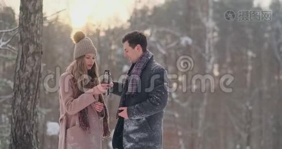 情侣在冬天的森林里喝热水瓶里的茶。 冬天公园里穿外套的时髦男女视频
